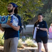 2 GVSU alumni carrying a case of water bottles and a mirror into the dorm building